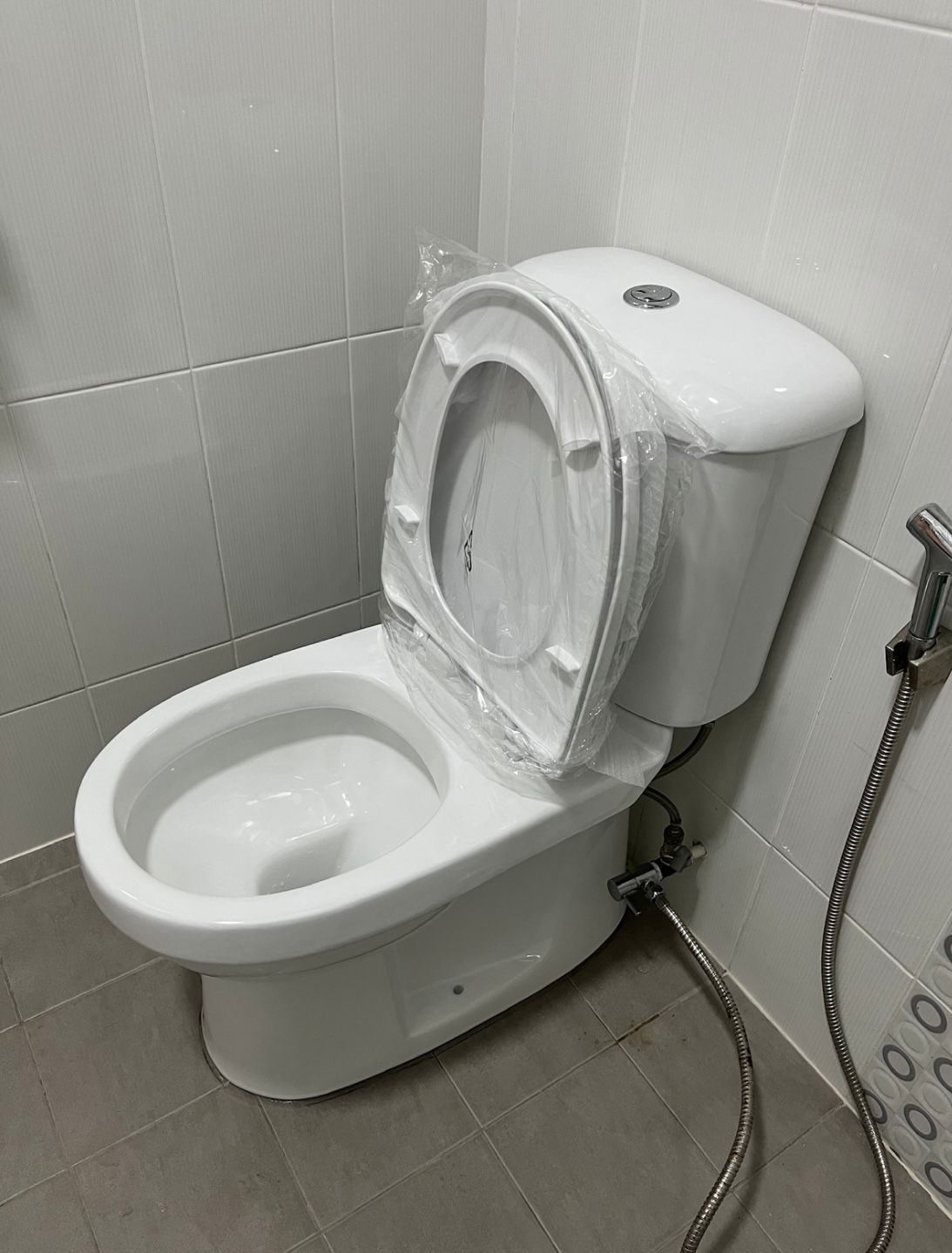 A brand new toilet installed, seat still in its factory wrapping